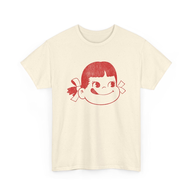 A flat lay of a cream-colored t-shirt with a red graphic of a girl's face with pigtails and a winking expression.