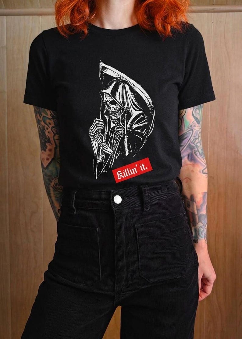 A person wearing a black t-shirt with a white grim reaper graphic and a red rectangular label with white text.