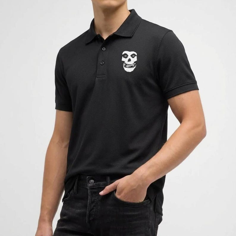 Close-up of a person wearing a black polo shirt with a white embroidered skull on the left chest and dark jeans.