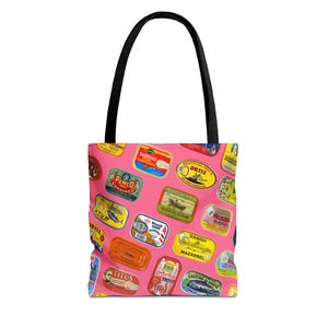 A pink tote bag with a pattern of colorful sardine can labels is displayed flat against a white background.