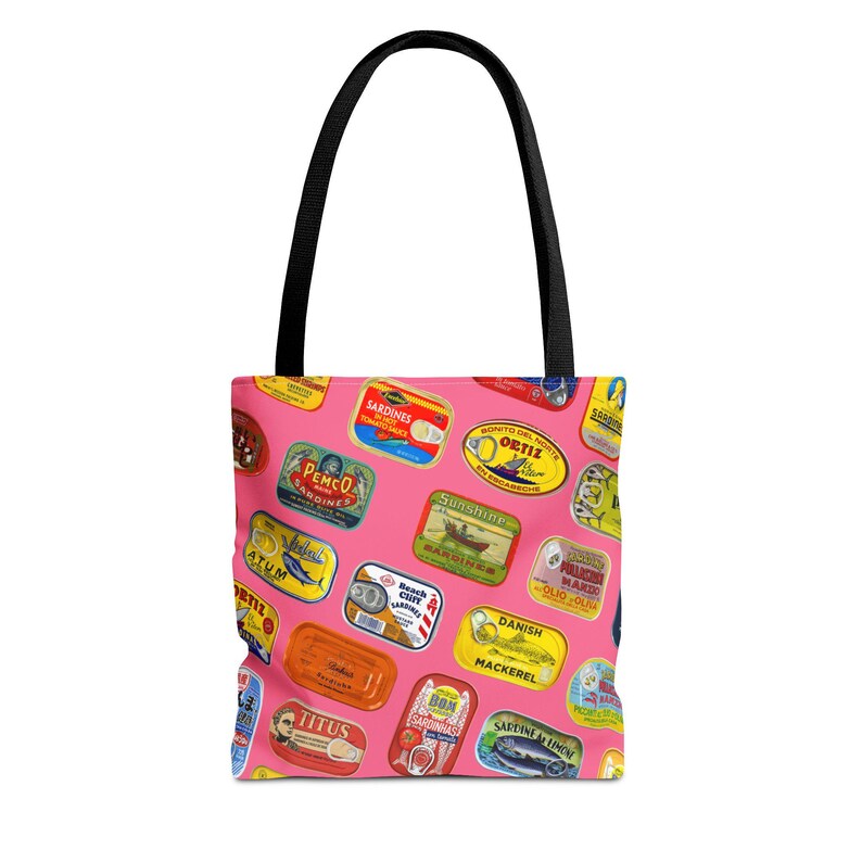 A pink tote bag with a pattern of colorful sardine can labels is displayed flat against a white background.