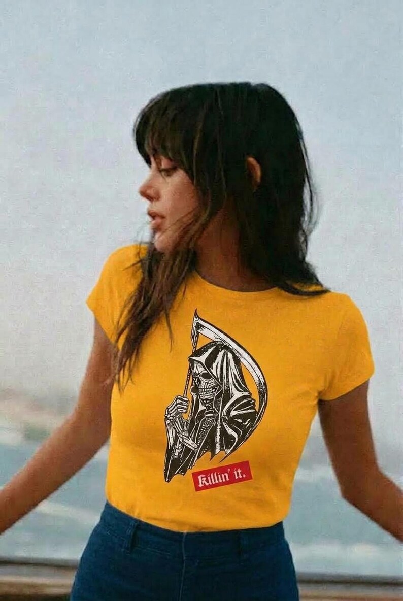 A person wearing a yellow fitted t-shirt with the grim reaper graphic and Killin it text, standing outdoors with a blurred background.