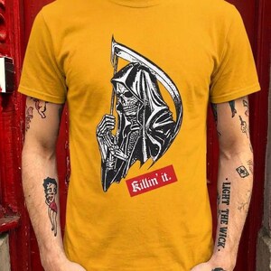 A person wearing a yellow graphic t-shirt featuring a grim reaper holding a scythe and red text.