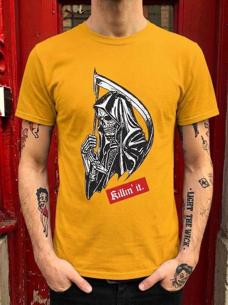 A person wearing a yellow graphic t-shirt featuring a grim reaper holding a scythe and red text.