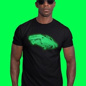 May include: A black short-sleeved t-shirt featuring a glowing neon green graphic of a vintage sedan car on the chest. The car illustration is rendered in a wireframe style, showing the front and side profile of the vehicle in a bright, luminous green hue.