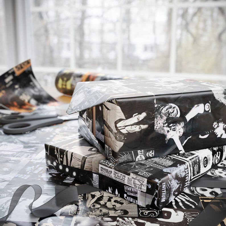 Two stacked gifts wrapped in black and white Misfits-themed paper, with loose paper and scissors on a table by a window.