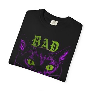 A neatly folded black t-shirt showing the top portion of the purple cat graphic and green text against a white background.