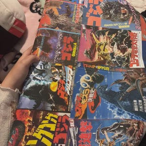 May include: A multi-panel poster featuring various Godzilla movie illustrations and Japanese text. The artwork displays Godzilla in different combat scenes against other monsters, with bold red and yellow Japanese typography throughout.