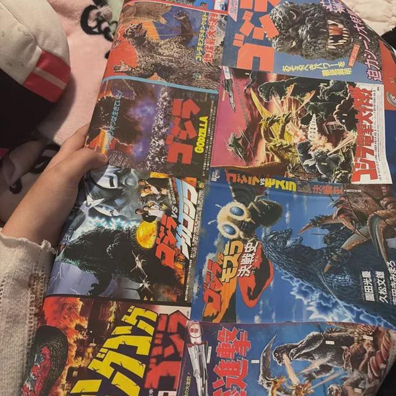 May include: A multi-panel poster featuring various Godzilla movie illustrations and Japanese text. The artwork displays Godzilla in different combat scenes against other monsters, with bold red and yellow Japanese typography throughout.