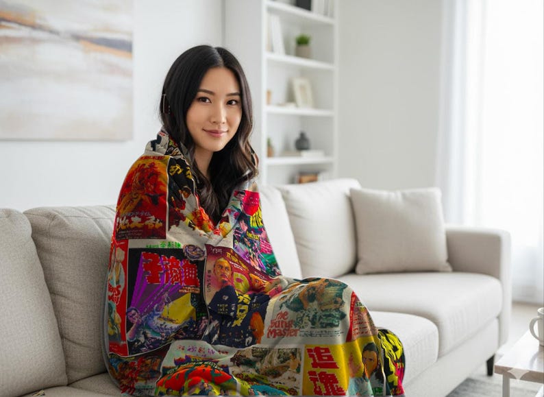 A woman sits on a light-colored sofa, wrapped in a blanket patterned with a collage of vintage Kung Fu movie posters.