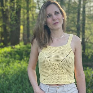 Peut inclure: Un d&eacute;bardeur en crochet jaune avec un motif carr&eacute;. Le haut est sans manches et a un col rond.