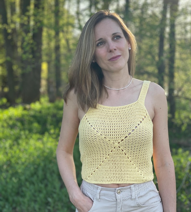 Peut inclure: Un d&eacute;bardeur en crochet jaune avec un motif carr&eacute;. Le haut est sans manches et a un col rond.