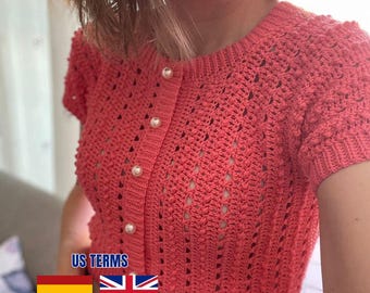 Peut inclure: Un gilet en crochet de couleur corail à manches courtes, doté d'un motif texturé en points noisette, d'une encolure ronde et d'une fermeture boutonnée sur le devant avec cinq boutons ronds en fausse perle blanche, ainsi qu'un ourlet côtelé.