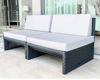 May include: A modern outdoor loveseat with a dark gray woven base and light gray cushions. The two-seater sofa has a rectangular shape and is placed on a light-colored tiled surface. The backrests are upright and the cushions are square.