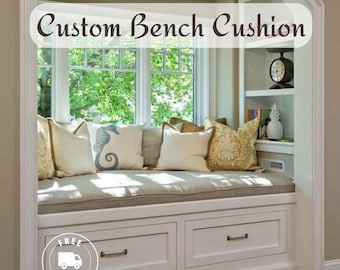 May include: A white window seat with a beige cushion and pillows. The seat has two drawers and is built into a bay window. The text "Custom Bench Cushion" is displayed above the window.