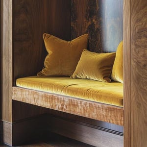 May include: A built-in wooden bench featuring a rich, dark wood grain frame and a plush, mustard-yellow velvet seat cushion. Three matching mustard-yellow velvet throw pillows are arranged along the back of the bench, set within a recessed nook.