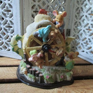 Può includere: Una statuetta stravagante di una ruota idraulica a forma di teiera, con diverse figure di topi. La teiera è color crema con un camino di mattoni rossi. La ruota idraulica è marrone chiaro e la base è marrone scuro con accenti verdi e rosa.