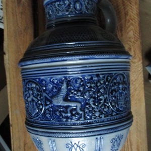 May include: A blue and white ceramic pitcher with intricate floral and animal designs. The pitcher has a lid and a handle.