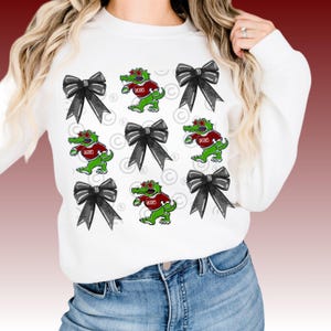 May include: White sweatshirt with a repeating pattern of black bows and green alligators wearing red shirts with the word "GATORS" printed on them.