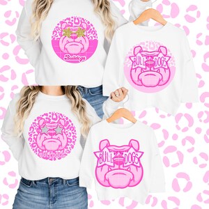 May include: Three white shirts with pink and gold bulldog designs. The designs feature a bulldog with star-shaped sunglasses and the text "Bulldogs".