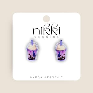 Op de afbeelding: Een paar hypoallergene oorbellen met een paars en wit bubble tea-ontwerp. De oorbellen zijn gelabeld "nikki doodles".