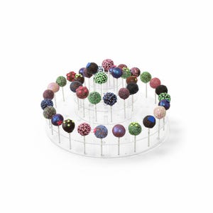 May include: A tiered, clear plastic cake pop stand filled with colorful cake pops. The cake pops are round and decorated with sprinkles, glitter, and various colors, including pink, blue, green, and brown.