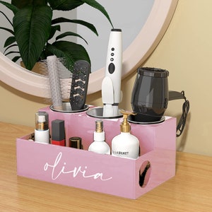 May include: Pink acrylic organizer with compartments for hair styling tools and bottles. The organizer has a label that says "olivia".