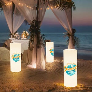 Puede incluir: Tres faroles luminosos cilíndricos blancos con un gráfico azul y amarillo que dice "Summer Party" en un entorno de playa.