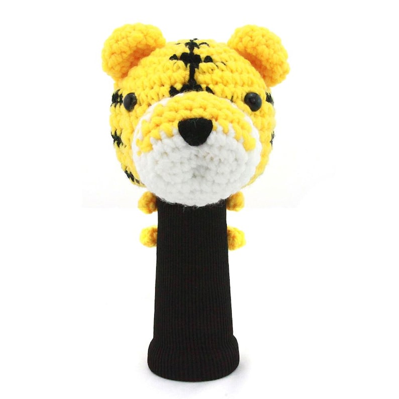 K&ouml;nnte beinhalten: Eine gelb-schwarze Golfschl&auml;gerhaube in Form eines Tigers. Die Haube zeigt ein Tigergesicht mit schwarzen Streifen, einer wei&szlig;en Schnauze und schwarzen Augen. Sie hat einen schwarzen Strickstrumpf zum Schutz des Golfschl&auml;gers.