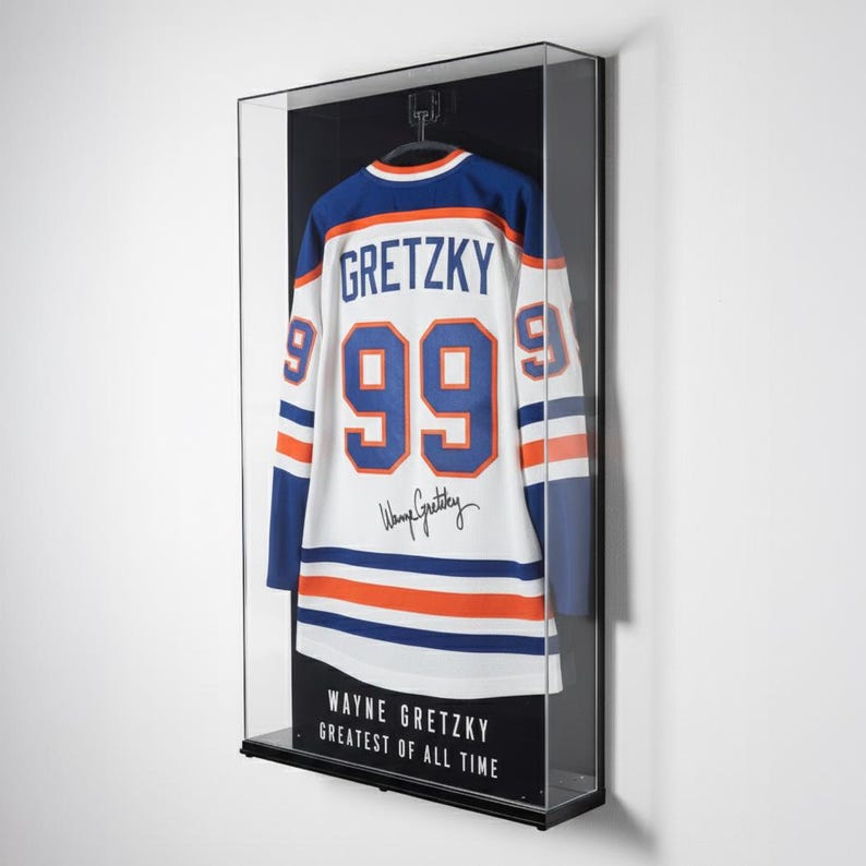 Puede incluir: Una camiseta de hockey enmarcada con el nombre "GRETZKY" y el n&uacute;mero "99" en la espalda. La camiseta es blanca con detalles azules y naranjas. El marco incluye el texto "WAYNE GRETZKY GREATEST OF ALL TIME".