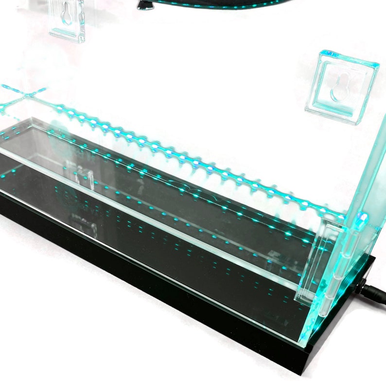 May include: A modern, rectangular aquarium with a black base and clear glass sides. The aquarium features a series of small, blue LED lights along the top edge and inside the tank. The design includes a clear, removable top and a power cord.