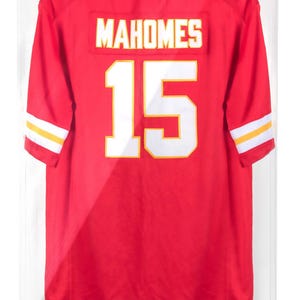 Puede incluir: Camiseta roja de los Kansas City Chiefs con el nombre "MAHOMES" y el n&uacute;mero 15 en blanco. La camiseta se exhibe en una vitrina. Las mangas tienen rayas blancas y amarillas. Texto "PATRICK MAHOMES #15 KANSAS CITY CHIEFS" en la parte inferior.
