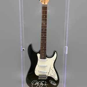 May include: Black and white electric guitar in a clear display case. The guitar has a signature on the body and the text "JON BON JOVI SLIPPERY WHEN WET TOUR JULY 1986" at the base. The case has a black base and a light.