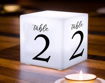 May include: White cube table number with black text that reads "Table 2". The cube is lit from within and glows.