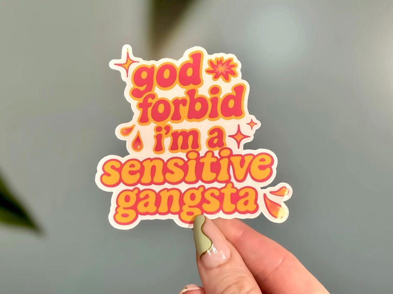 K&ouml;nnte beinhalten: Ein wei&szlig;er Aufkleber mit dem Text "god forbid i'm a sensitive gangsta" in orangefarbenen und rosa Buchstaben. Der Aufkleber hat eine Retro-&Auml;sthetik mit Sternen und Glitzer.