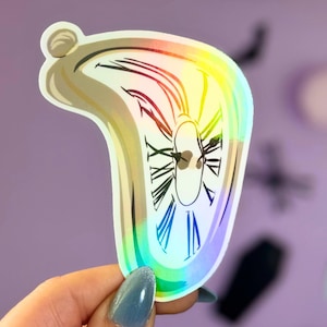 May include: A holographic sticker of a melting clock, a popular surrealist image. The sticker is rainbow iridescent and features a black and white clock face.