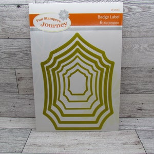May include: A package of badge label die templates. The package has a white background with the words "Fun Stampers Journey" and "Badge Label" printed on it. The die templates are gold and are in a nested badge shape.