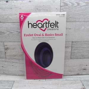 Puede incluir: Un paquete de troqueles artesanales Heartfelt Creations Eyelet Oval & Basics Small. El paquete es blanco y rosa, con un logotipo en forma de corazón y el texto "Eyelet Oval & Basics Small". Contiene seis piezas.