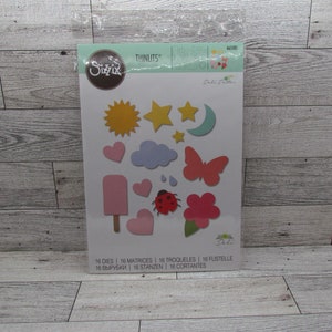 Puede incluir: Un paquete de troqueles Sizzix Thinlits con varias formas, incluyendo un sol, estrellas, luna, corazones, nubes, gotas de lluvia, una mariposa, una mariquita y una flor. Los troqueles son en tonos amarillos, rosas y azules. El paquete también incluye el texto "16 DIES | 16 MATRICES | 16 TROQUELES | 16 FUSTELLE".