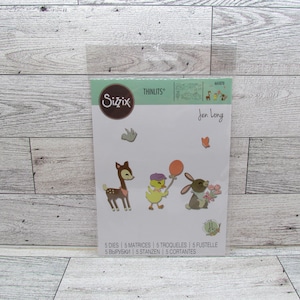 May include: A Sizzix Thinlits die set with animal designs, including a deer, duckling, and bunny. The packaging features the designer's name, Jen Long, and the text "5 DIES | 5 MATRICES | 5 TROQUELES 5 FUSTELLE". The dies are ideal for crafting projects.