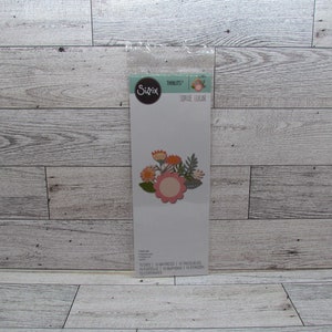 Puede incluir: Un paquete de troqueles Sizzix Thinlits con un diseño floral de Sophie Guilar. Los troquelados incluyen una flor rosa central con borde festoneado, rodeada de elementos florales naranjas, amarillos y verdes. Contiene 15 troqueles.