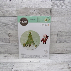 May include: A package of Sizzix Thinlits dies for Christmas crafting. The package features a circular design with a Christmas tree, snowman, and gifts. A Santa Claus figure is also included. The package includes 8 dies.