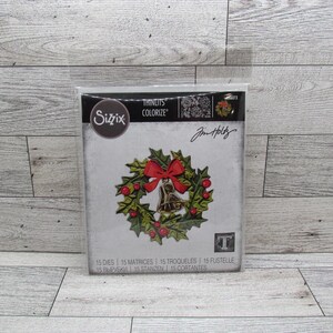 May include: A Sizzix Thinlits die set for crafting, featuring a Christmas wreath design with a red bow, berries, and a bell. The package includes the text "Jim Holtz".