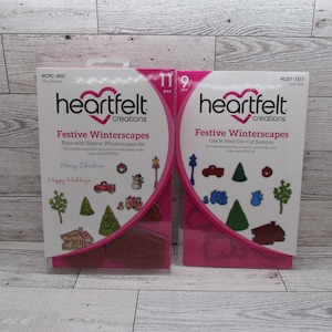 May include: Two Heartfelt Creations Festive Winterscapes craft sets. One set includes 11 pieces of cling stamps, and the other includes 9 craft dies. The packaging features a pink and white design with winter-themed illustrations and the text "Merry Christmas" and "Happy Holidays."
