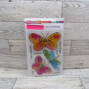 May include: Clear stamps featuring colorful butterfly designs. The stamps include phrases like "thank you," "happy birthday," and "my friend." The package is labeled "FransFormers" and "STAMPENTOUS!"