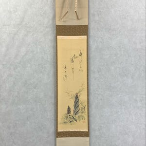 May include: A traditional Japanese scroll painting featuring a bamboo plant illustration with calligraphy. The artwork is primarily beige, brown, and green, with a cream-colored top and bottom. The scroll is suspended from a black rod.