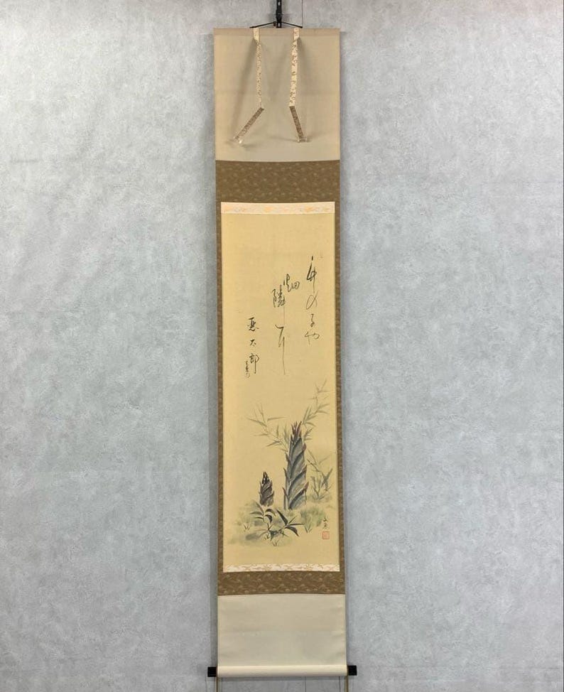 May include: A traditional Japanese scroll painting featuring a bamboo plant illustration with calligraphy. The artwork is primarily beige, brown, and green, with a cream-colored top and bottom. The scroll is suspended from a black rod.