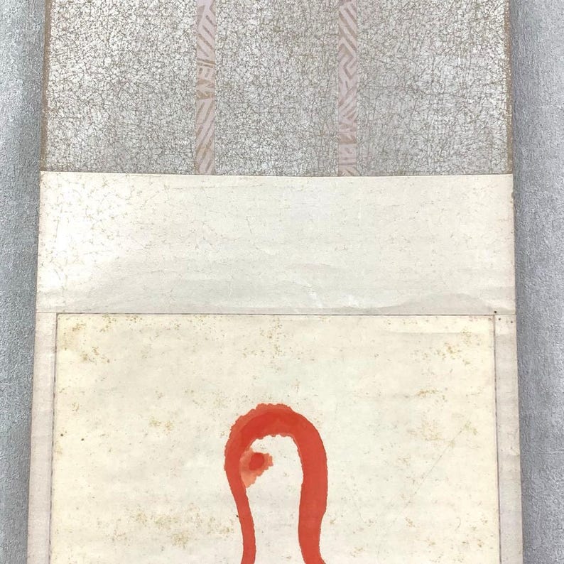 May include: An abstract artwork featuring a red, curved shape on a cream-colored background. The top portion has a textured, gray surface with vertical pink stripes. The artwork is framed with a light-colored border.