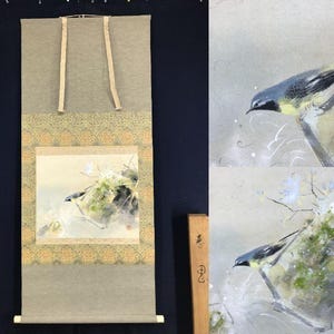 May include: A Japanese scroll painting depicting a bird on a branch. The artwork is a detailed watercolour painting with a muted colour palette, including shades of grey, green, and yellow. The scroll has a neutral-toned background with decorative borders.