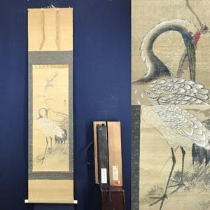 Peut inclure: Peinture sur rouleau japonaise représentant deux grues dans un cadre naturel. L'œuvre utilise principalement des tons beige, gris et noir, avec une touche de rouge. Le rouleau est monté sur un support crème avec une bordure bleu foncé.